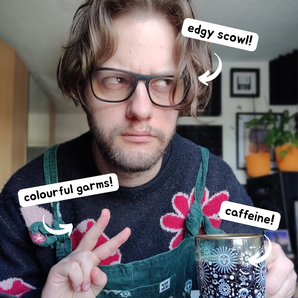 Luke scowling and throwing a peace sign to the camera while he holds a cup of coffee. He is wearing dunagrees and a jumper covered in flower and mushroom print. Text popouts on the image point to different picture features. #1 reads 'Edgy Scowl', #2 reads 'Colourful Garms!' #3 reads 'caffeine!'